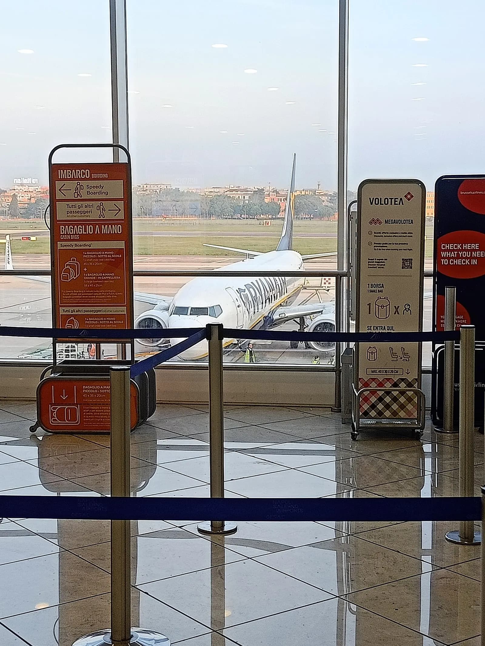 Departures window at Naples Capodichino with Ryanair jet and Napoli Salerno Airports barriers