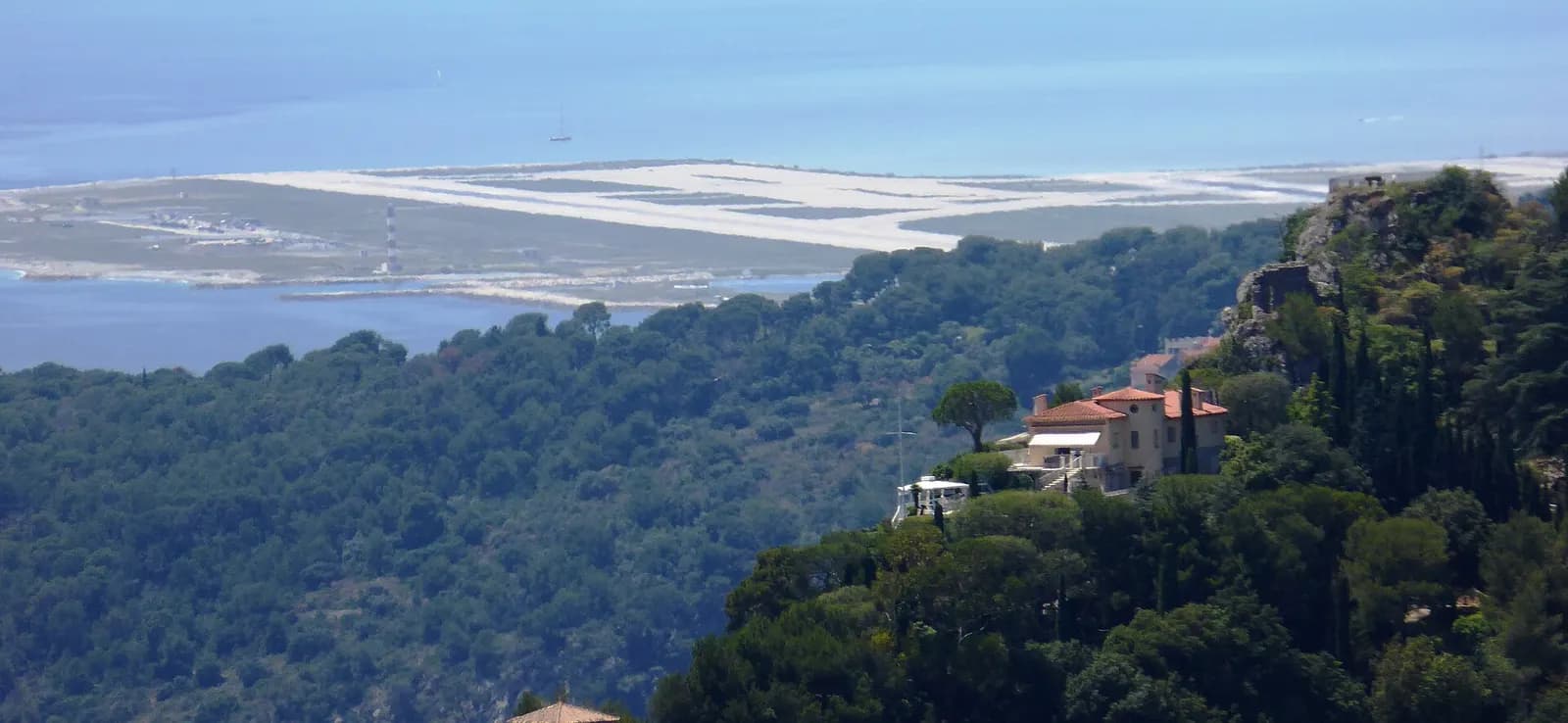 Wide panoramic view from Èze across the French Riviera coastline, with Nice Côte d'Azur Airport visible along the shore below.