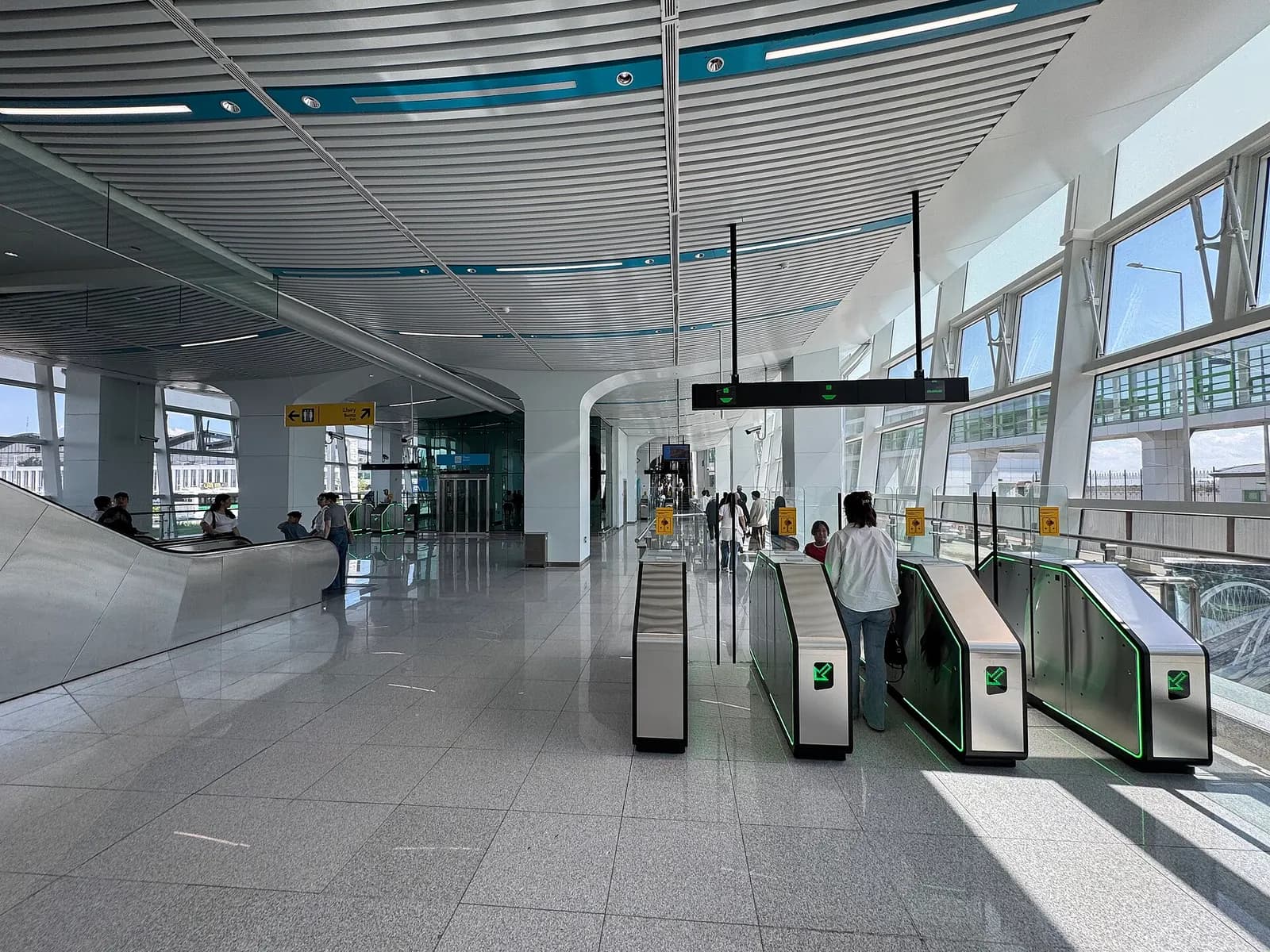 Interior view of the concourse at Airport Station, Nursultan Nazarbayev International Airport, featuring fare gates, escalator access, and elevated platform connection