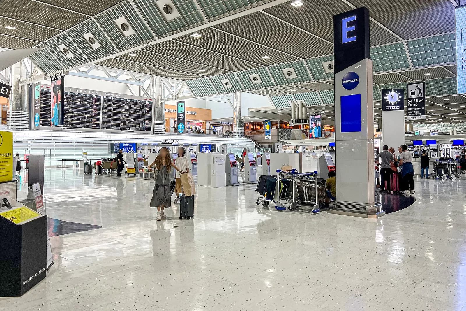 A long departure concourse in Terminal 2 with glass walls, retail shops, and passengers walking toward security and the gate areas.