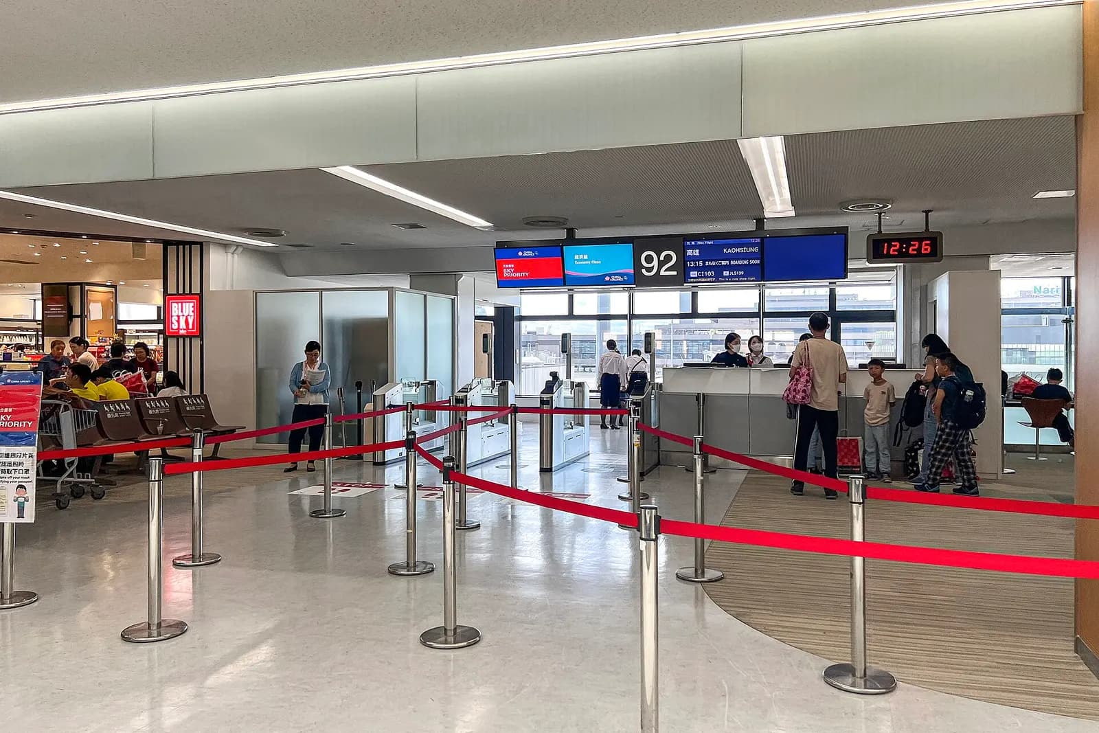 A boarding gate area in Terminal 2 labeled Gate 92 with passenger seating and an aircraft visible through the terminal windows.