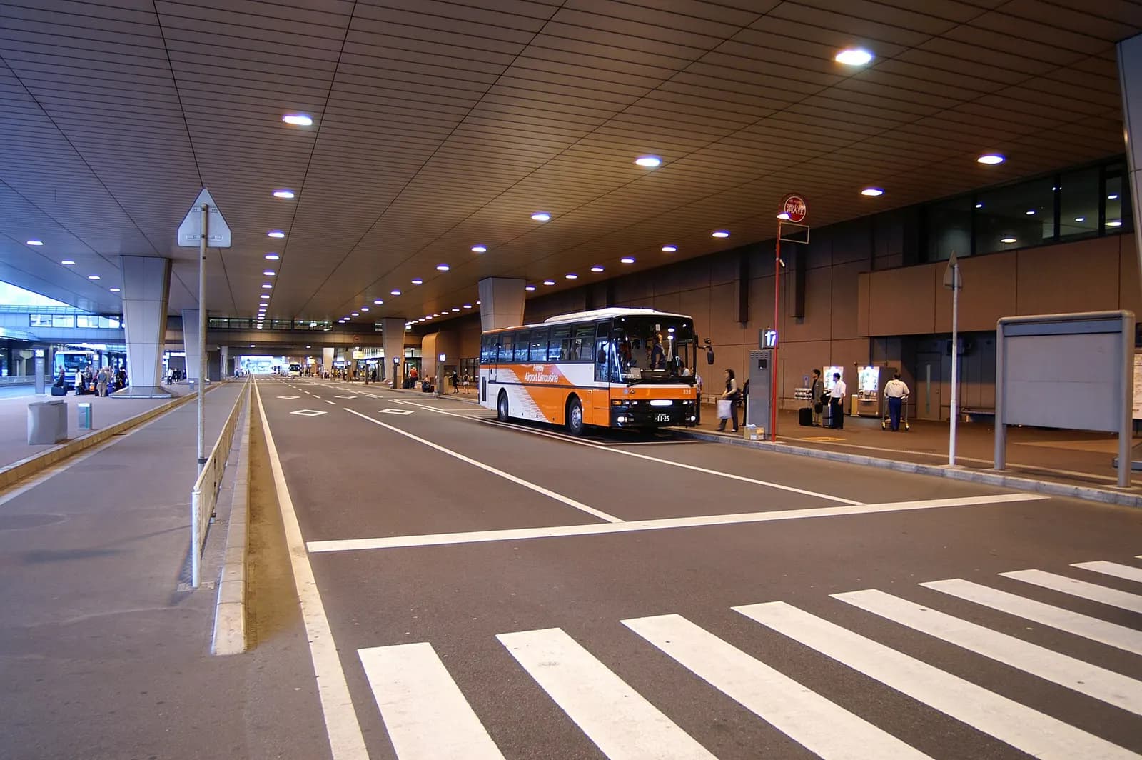 The curbside passenger drop-off zone outside Narita Terminal 2 with buses, taxis, and the terminal building façade in the background.