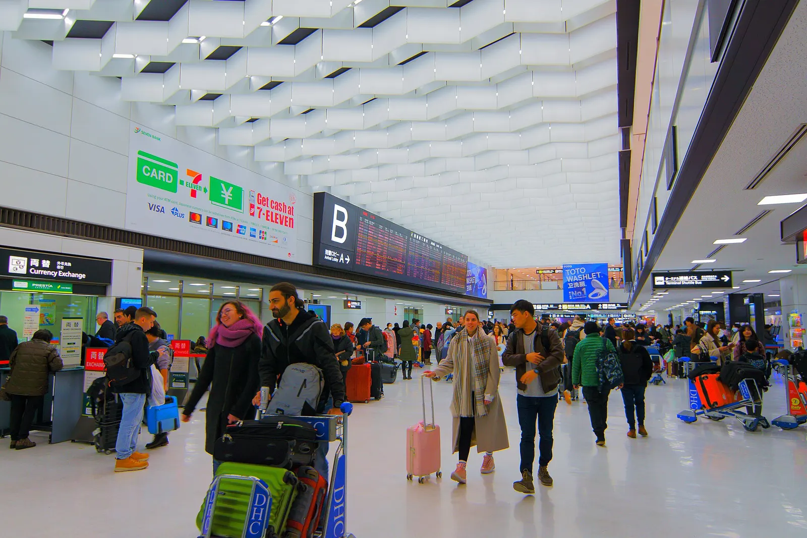 The wide, brightly lit arrival lobby of Terminal 2 with high ceilings, overhead signs, and travelers moving through the hall after landing.