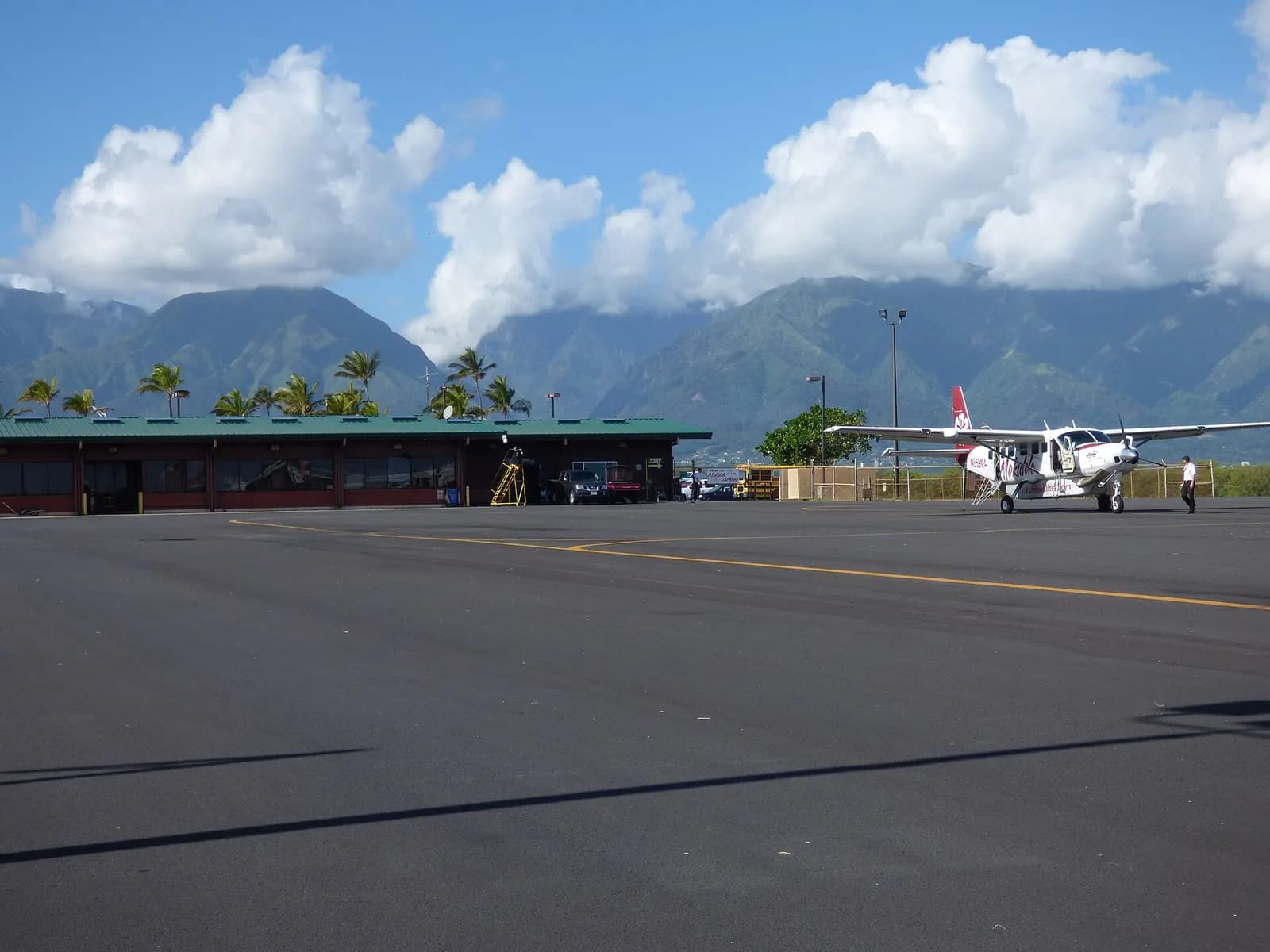 Kahului commuter terminal with a green-roof single-story hall and a Mokulele Cessna on the ramp, West Maui mountains behind.