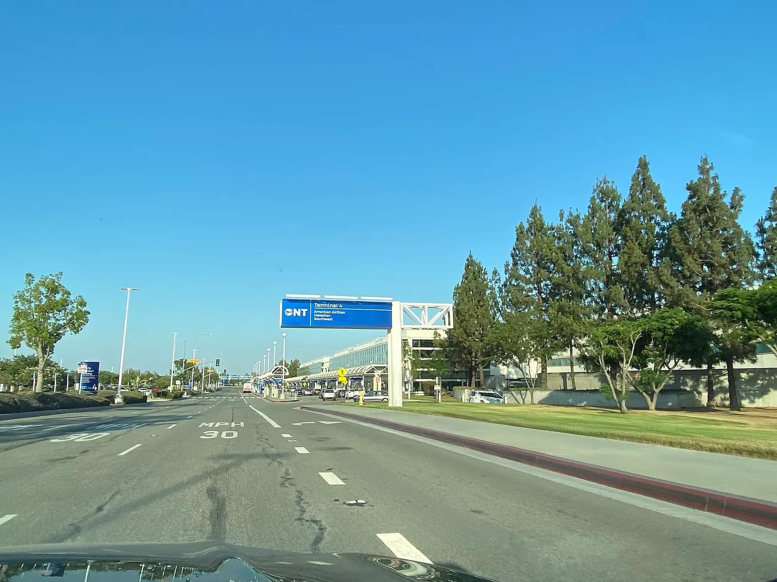 Roadside ONT sign for Terminal 4 listing American Airlines, Hawaiian, and Southwest under a clear sky.