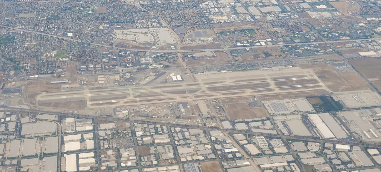 Aerial of Ontario International Airport showing two parallel east-west runways, north-side terminals, and surrounding Inland Empire warehouses.