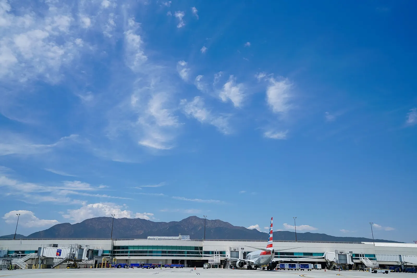 Airside Terminal 4 at Ontario International Airport with an American Airlines jet at Gate 408 and the San Gabriel Mountains behind the building.