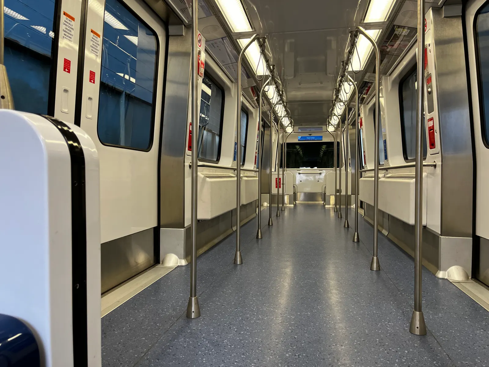 Inside a modern Airport Transit System car, blue seats and handrails line a clean cabin with doors at each end.