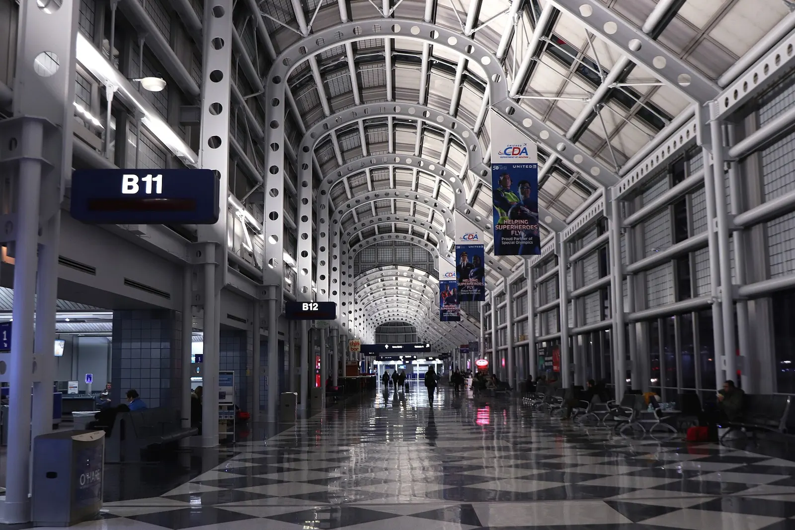 Passengers wait in a well-lit gate hold room at Terminal B gates B11 and B12 with a parked jet visible through the windows.