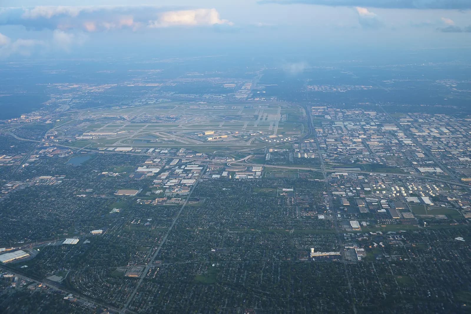 A wide aerial view shows Chicago O'Hare's sprawling runways, terminals, and ramp areas from an approaching passenger jet.