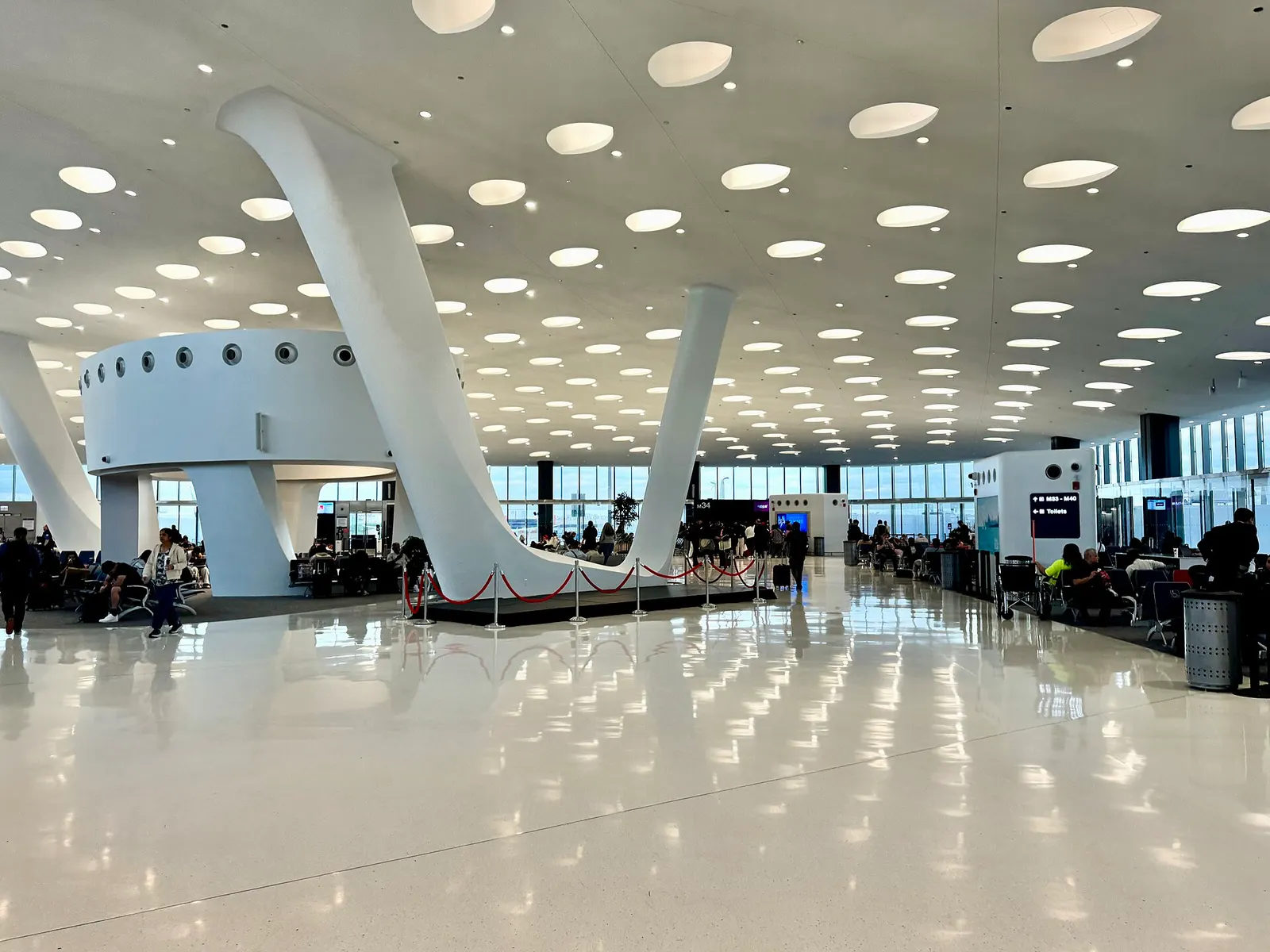 A long, glass-walled concourse in Terminal 5 stretches past gate seating areas and flight information displays.