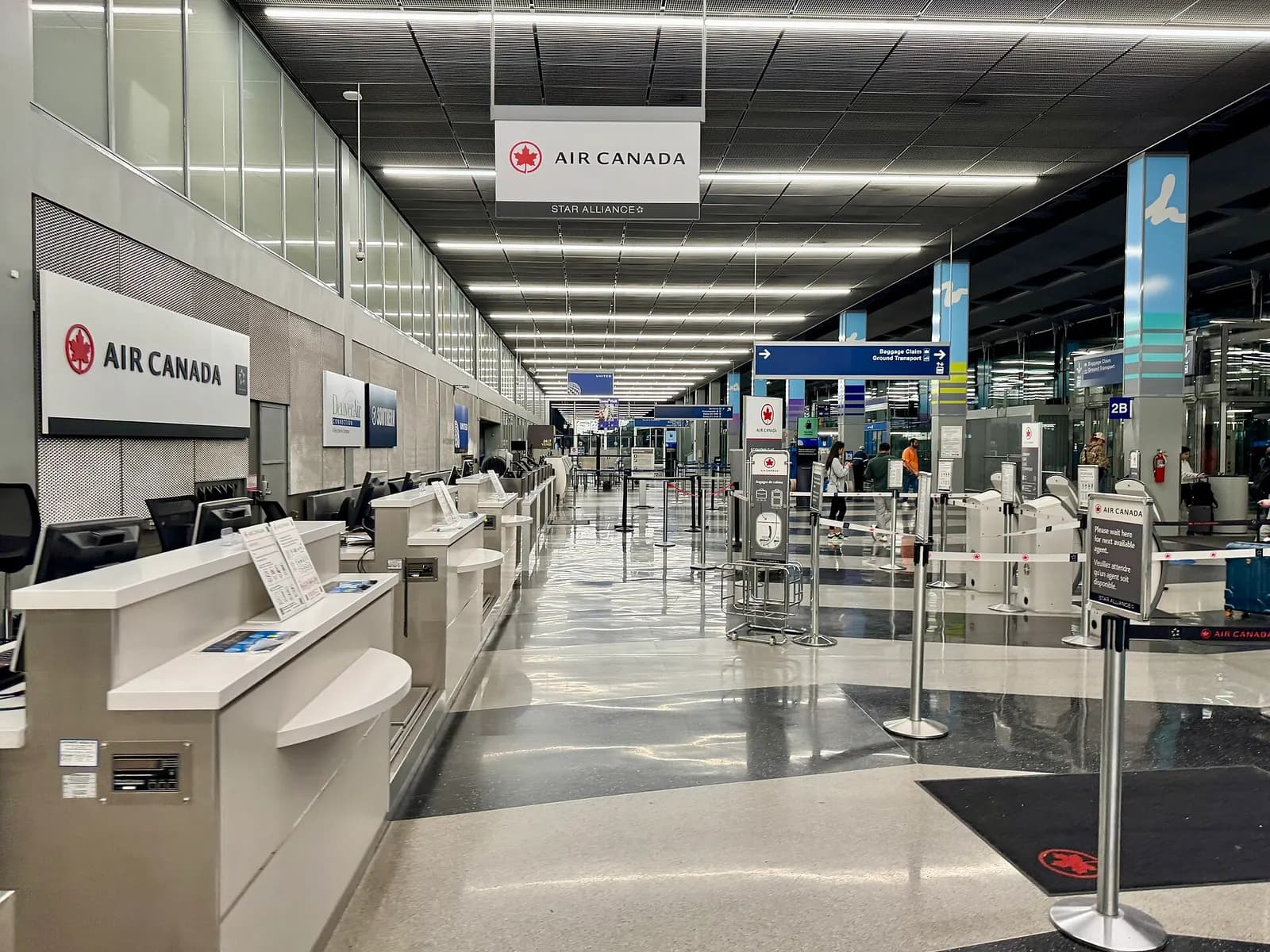 Travelers queue at airline check-in counters beneath a high ceiling in the Terminal 2 entrance hall.