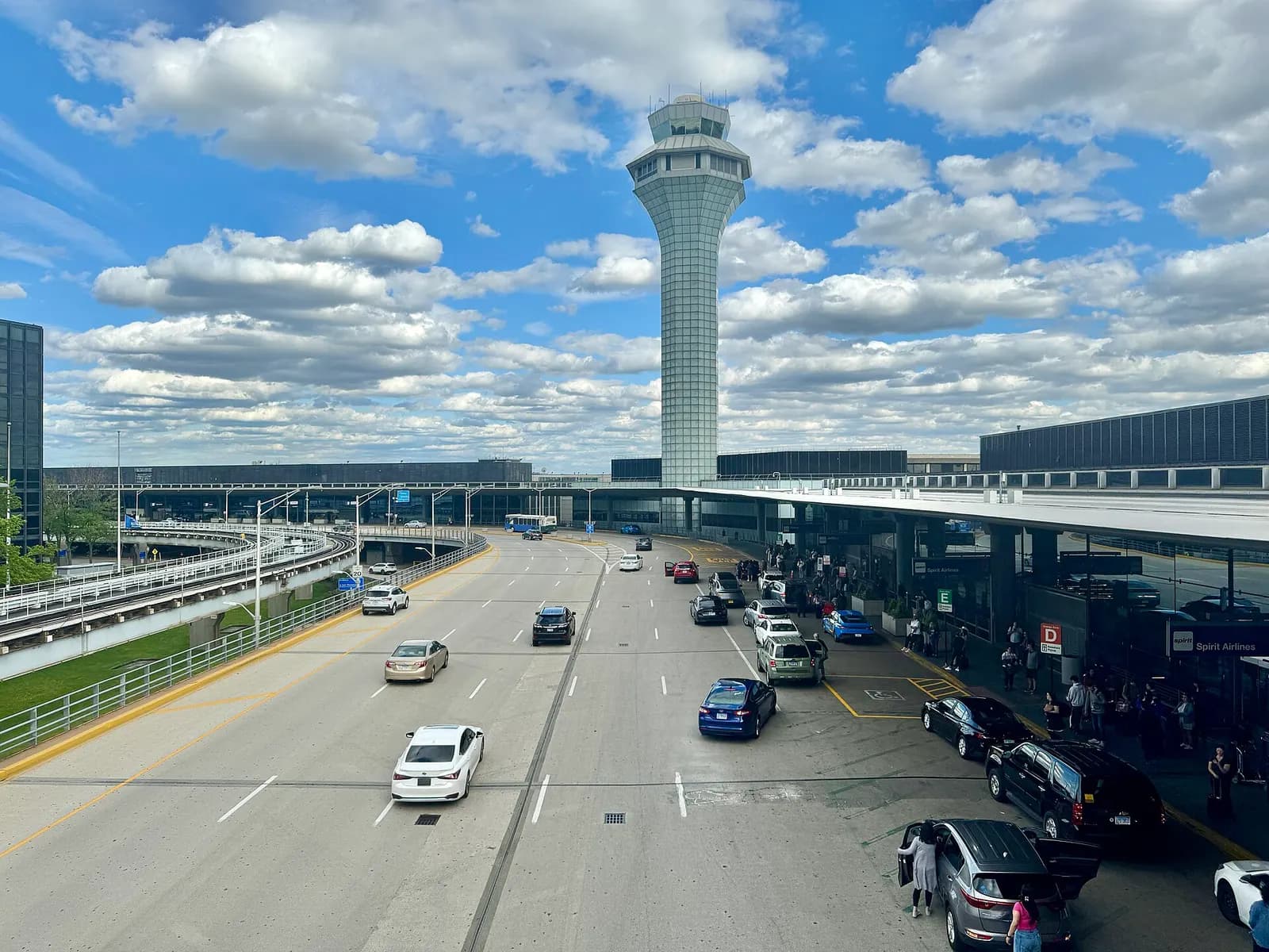 The curved glass-and-steel facades of O'Hare Terminals 2 and 3 rise above the roadway and landscaping on a clear day.