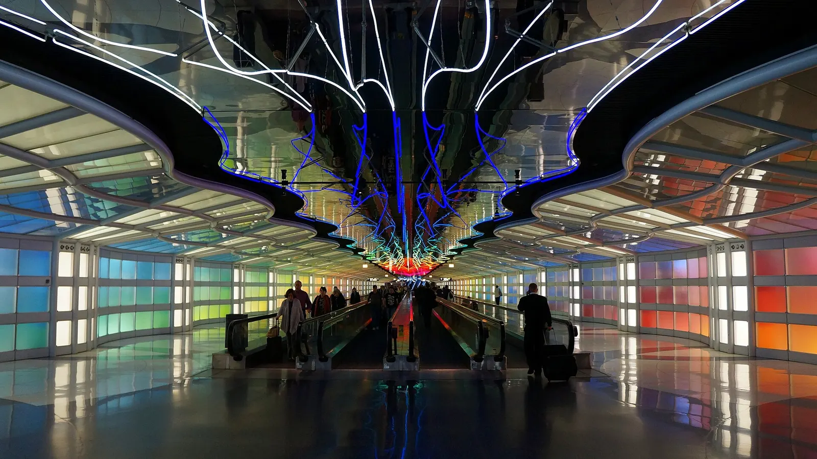 A neon-lit underground pedestrian tunnel with moving walkways connects sections of Terminal 1.