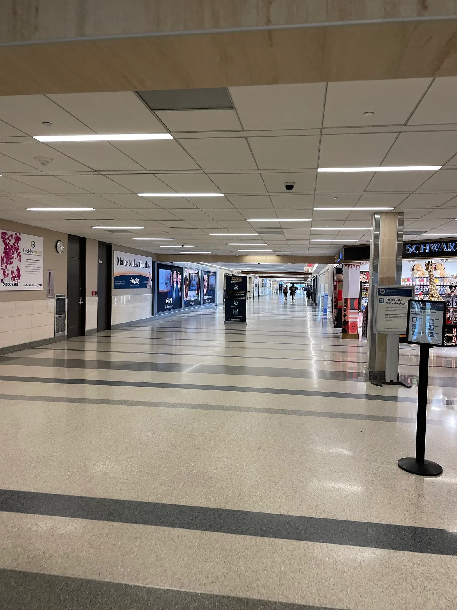 Long terrazzo concourse hallway at ORF with advertising lightboxes and a newsstand on the right.