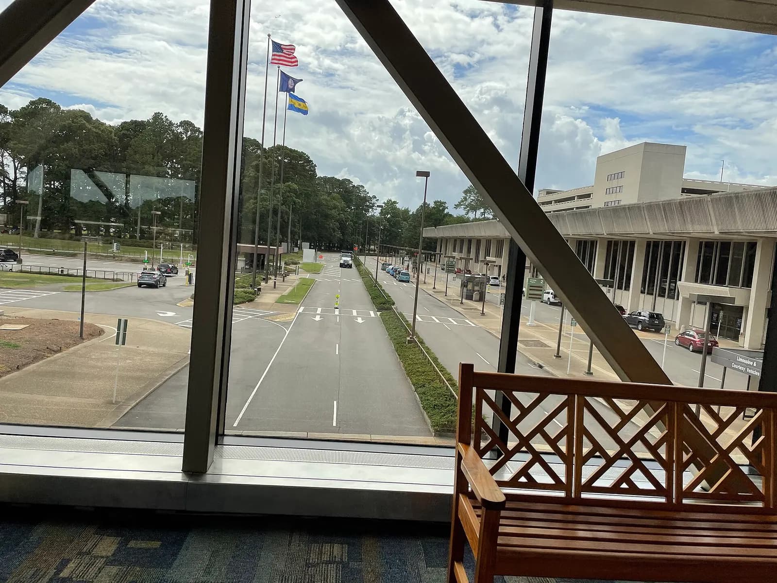 View from the pedestrian bridge toward the Arrivals Terminal roadway, flags, and parking garage.