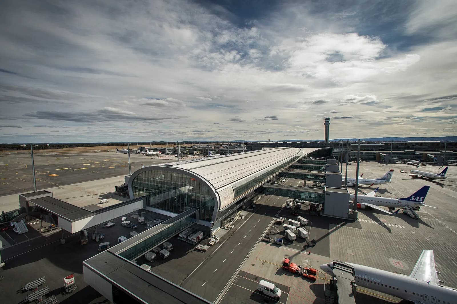 The long Pier North concourse at Oslo Airport with gate seating, floor-to-ceiling windows, and aircraft visible on the apron outside.