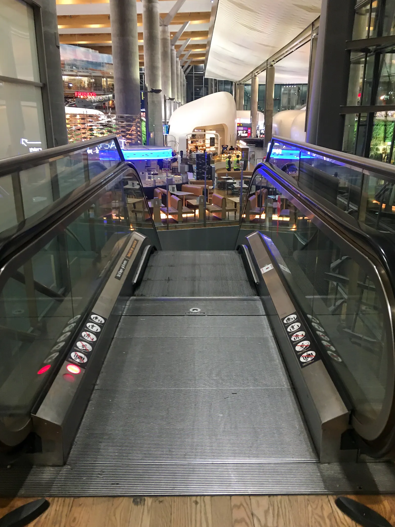 Passengers riding an escalator between levels inside Oslo Airport's terminal building.