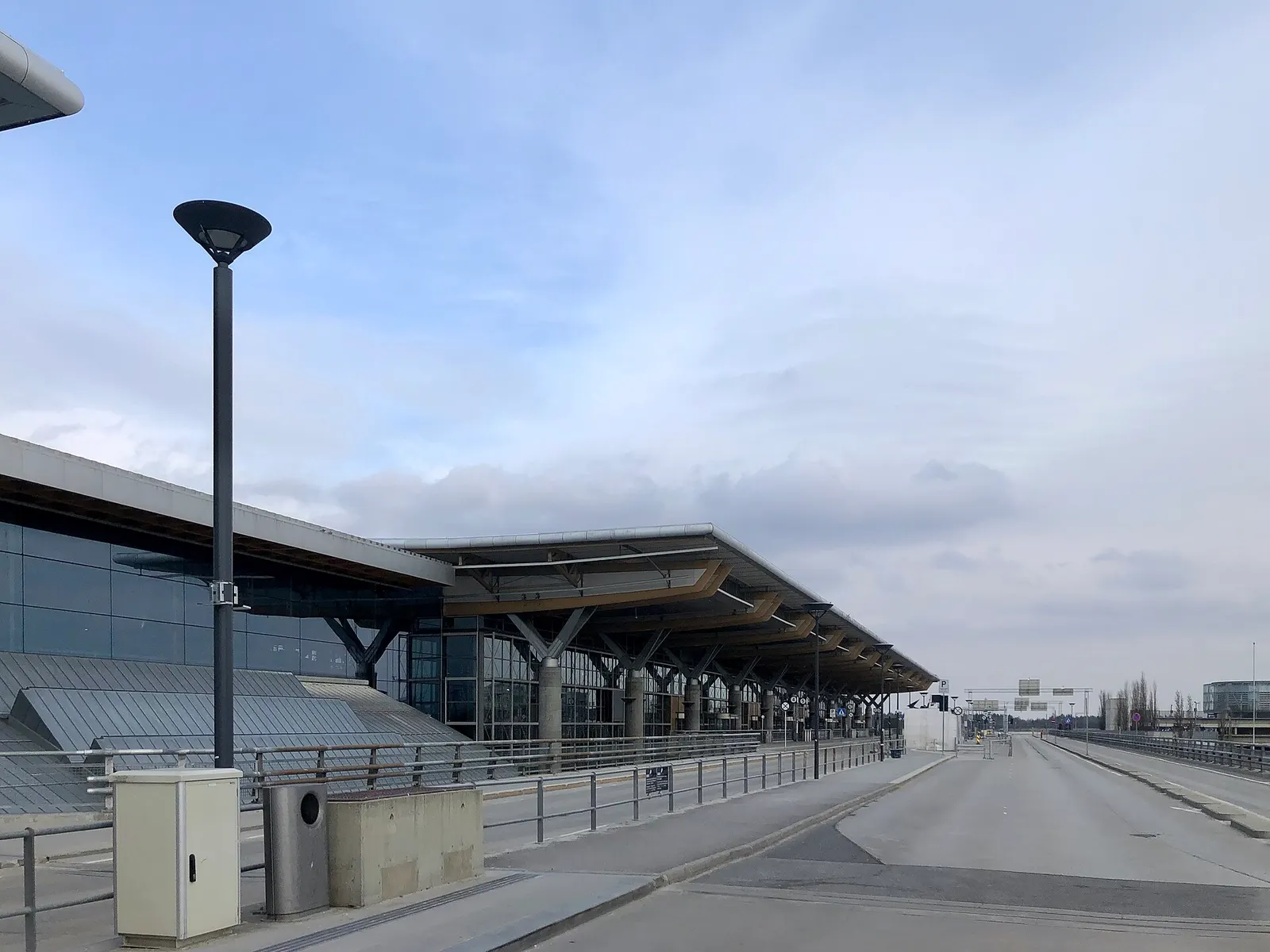 The covered passenger drop-off area outside Oslo Airport Gardermoen, with roadway lanes and the terminal entrance ahead.