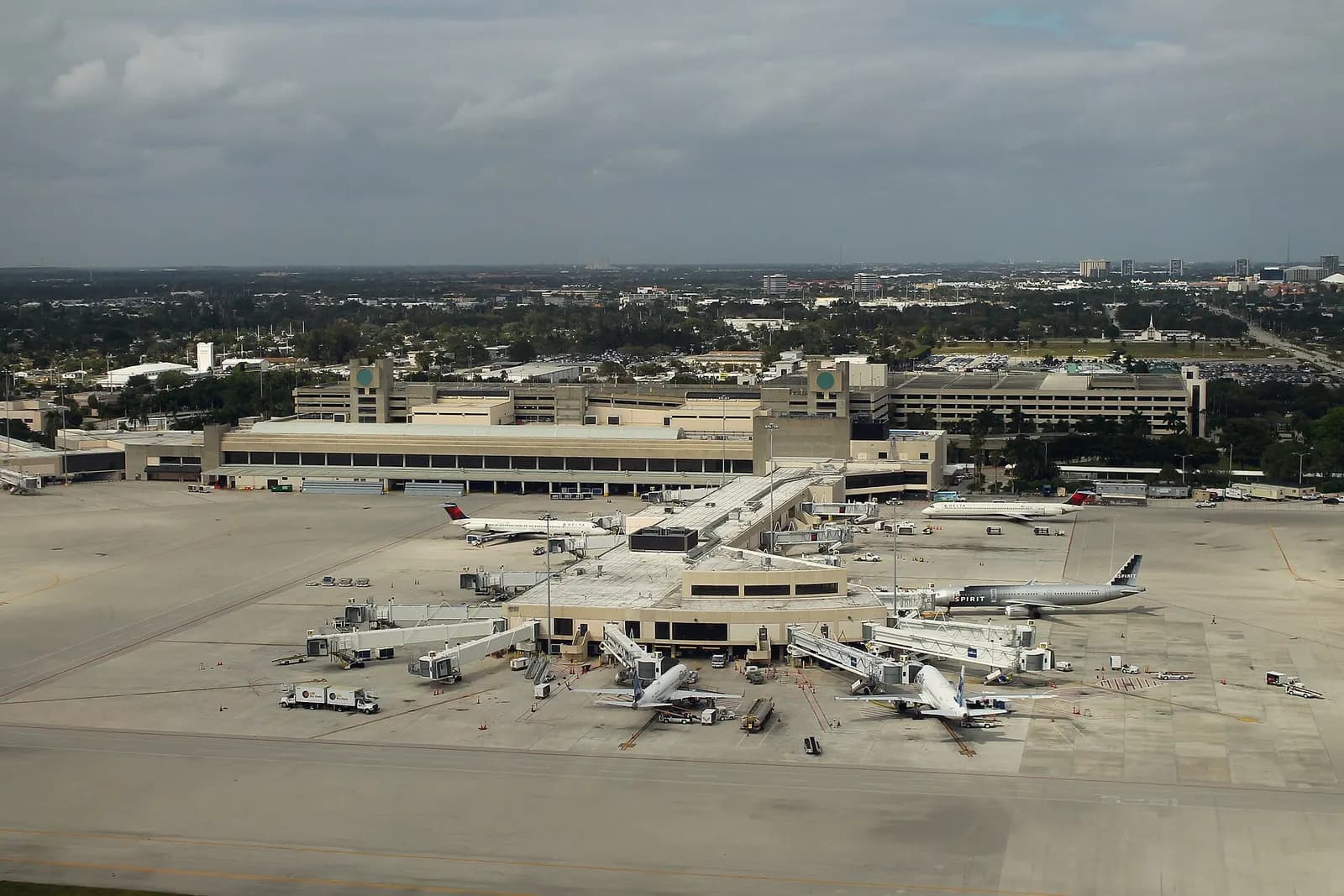 Aerial of Concourse C at Palm Beach International Airport with jet bridges, parked airliners, and the landside parking garage behind the finger.