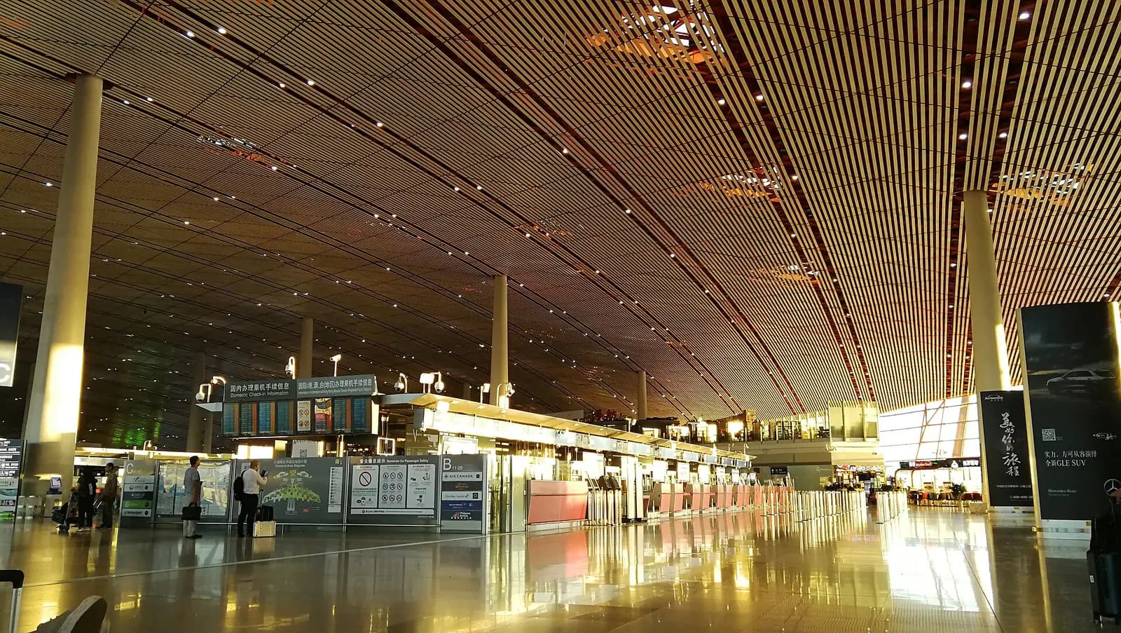 Spacious Terminal 3 departure hall with high ceilings, red support columns, and travelers walking beneath overhead flight information displays.
