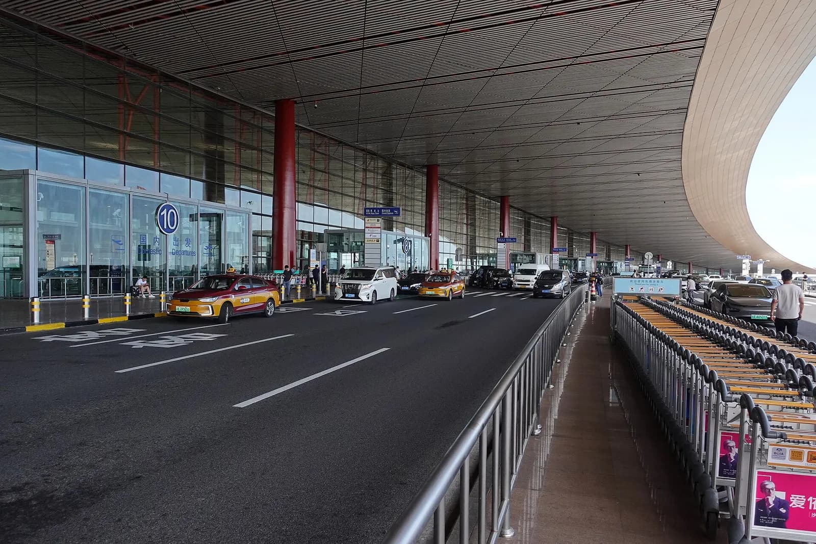 Exterior view of Terminal 3's main departure entrance with glass doors, curbside drop-off lanes, and the building's curved facade.