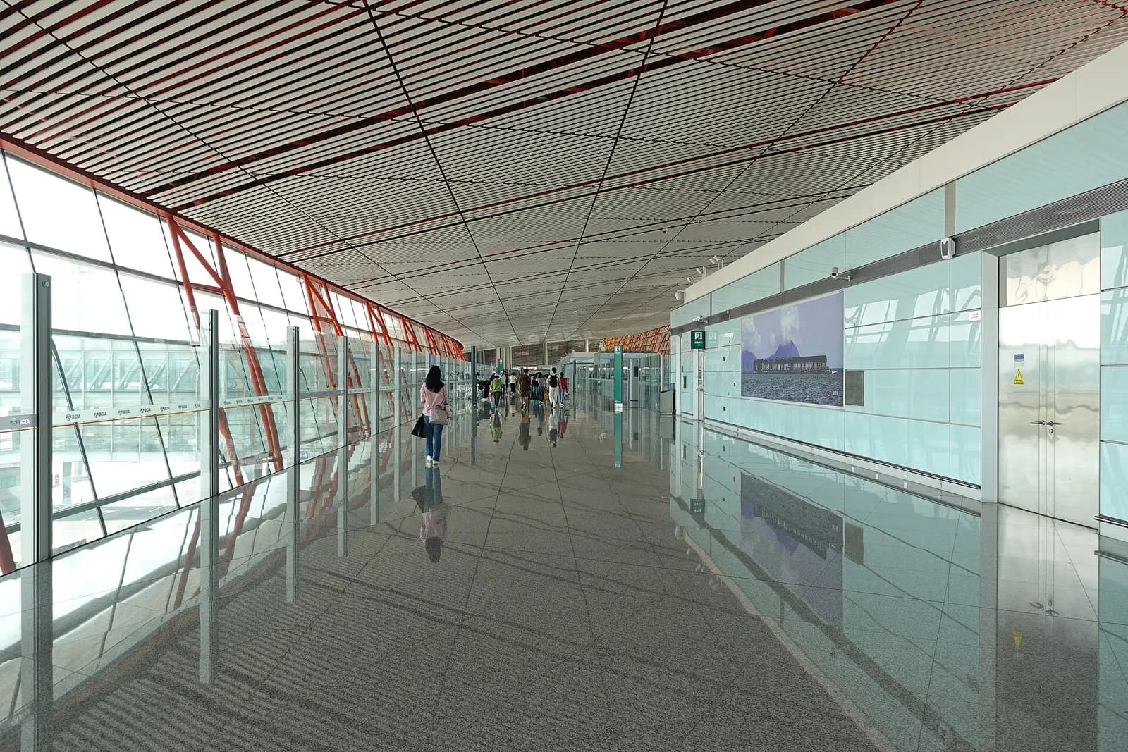 International arrivals hall in Terminal 3E with overhead signage, glass walls, and passengers walking toward exits and baggage claim.