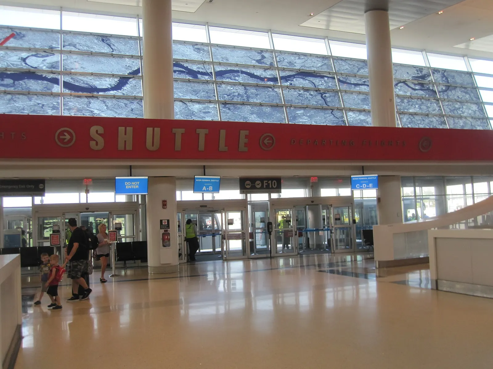 A marked shuttle-bus stop inside Terminal F with signage directing passengers to remote gates and terminal connections.