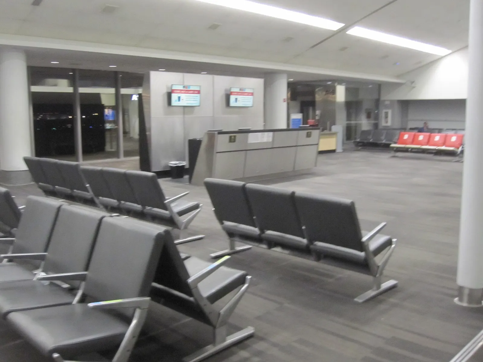 Rows of blue upholstered seats in a gate hold room in Terminal A, with large windows overlooking the airfield.