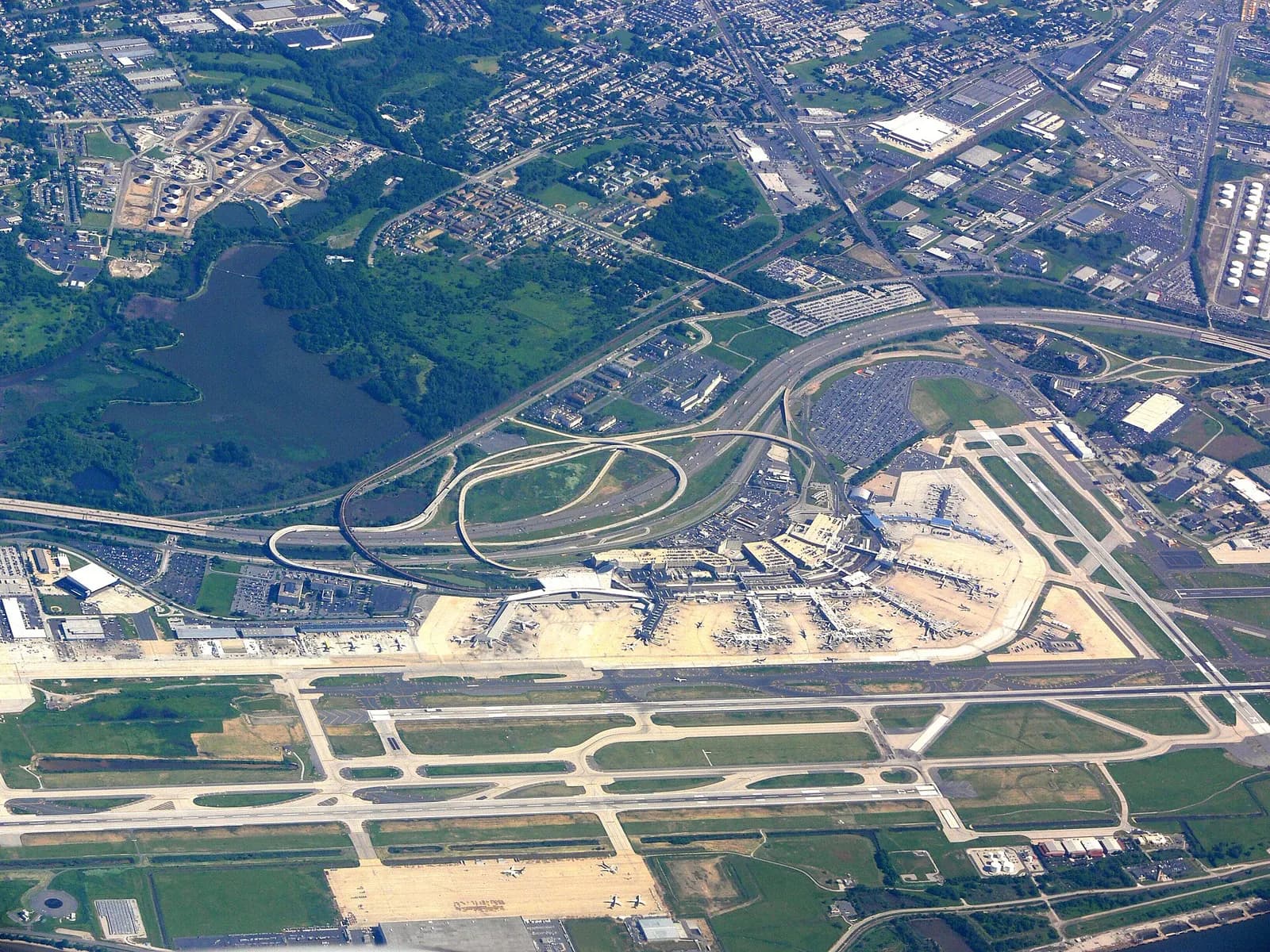 An aerial view shows Philadelphia International Airport's parallel runways, terminal buildings, and surrounding roads and parking areas.