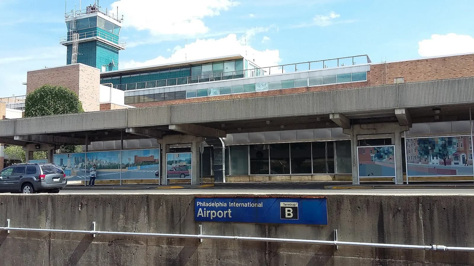 The curved facade of Terminal B at Philadelphia International Airport with the airport control tower rising behind it under a clear sky.