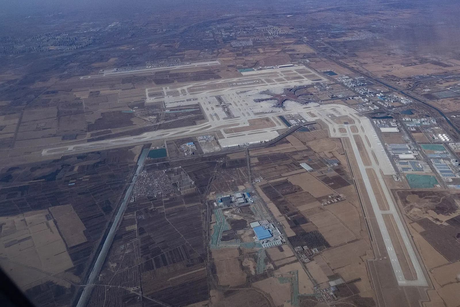 A wide panoramic aerial photograph of the full Beijing Daxing airport complex, runways, and surrounding landscape.