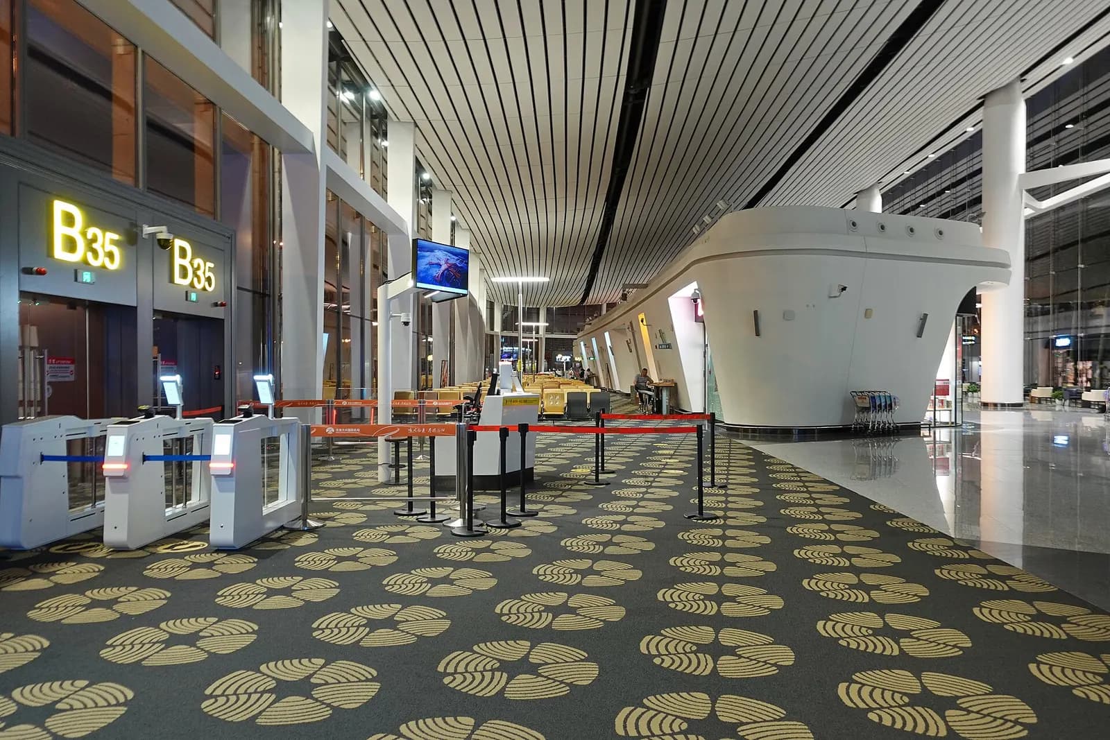 A departure gate area labeled B35 with seating, flight information displays, and a jet bridge leading to the aircraft.