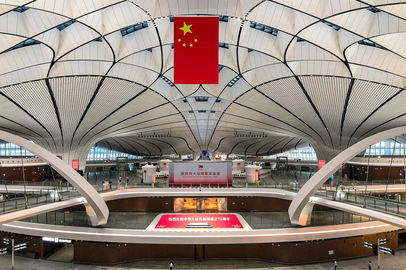 The soaring central atrium of the terminal with a curved white ceiling, tall columns, and a large Chinese flag hanging overhead.
