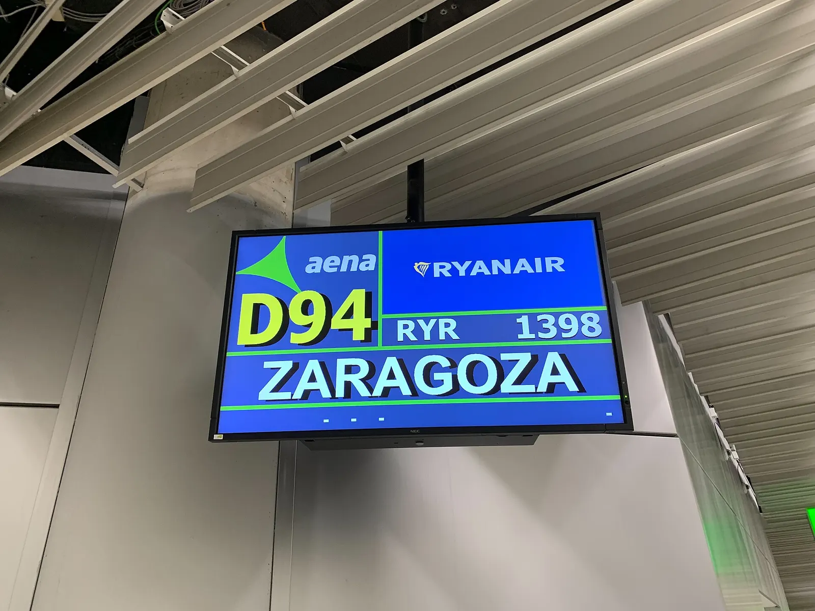 A wall-mounted flight information display in the terminal shows departure details for a flight to Zaragoza.