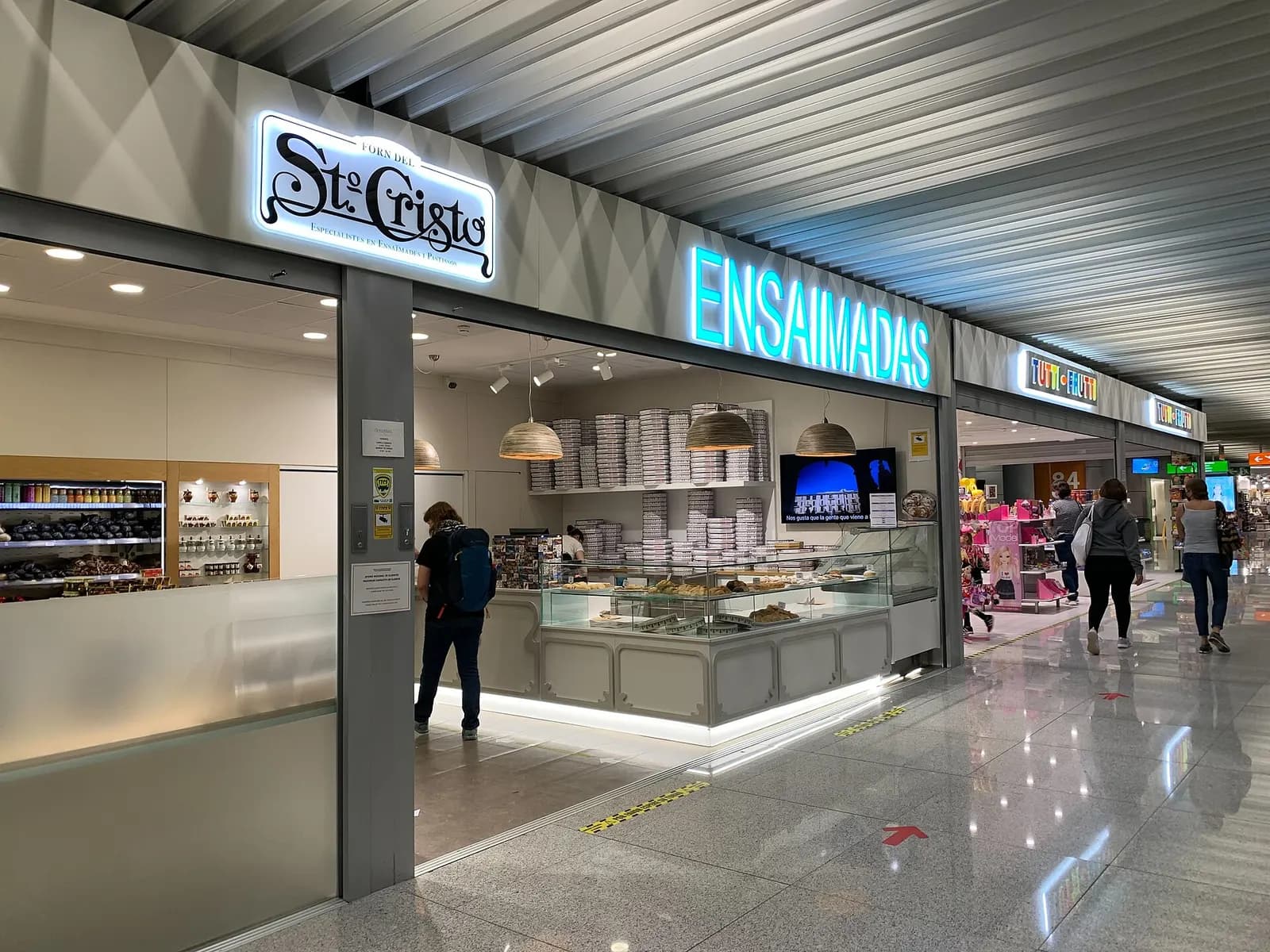 Shopfronts for Sto Cristo bakery and Tutti Frutti face a busy concourse walkway inside Palma de Mallorca Airport.