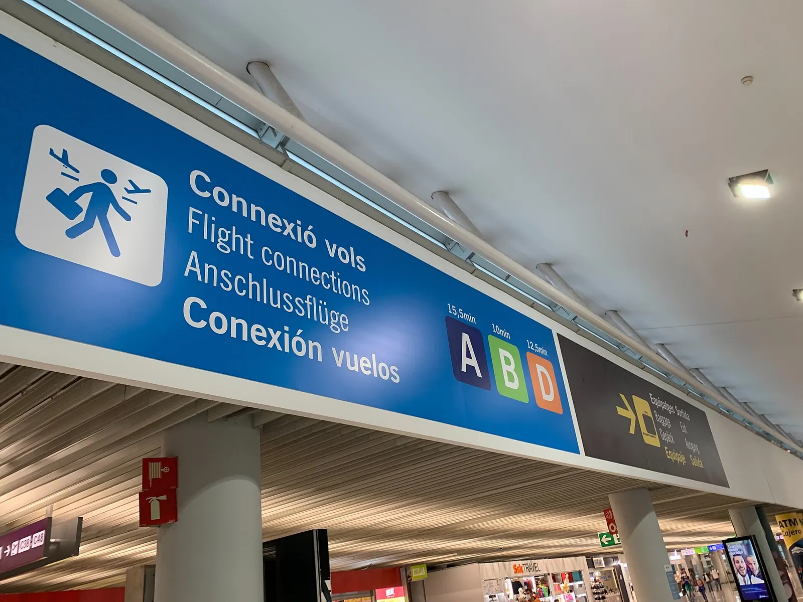Overhead directional signs in the terminal mark routes to flight connections, baggage claim, and exits at Palma de Mallorca Airport.