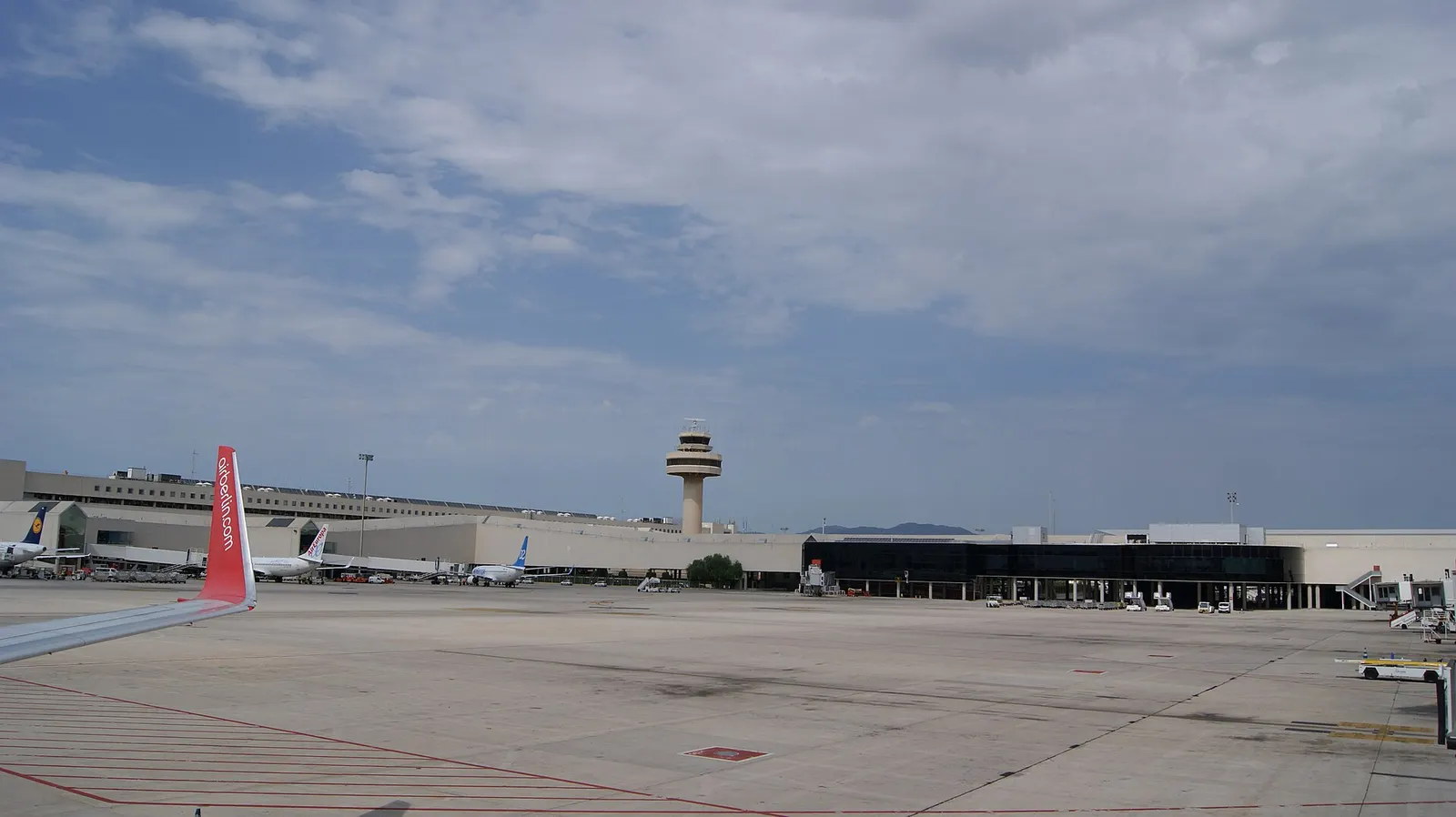 The airport control tower rises above runways, taxiways, and terminal buildings at Palma de Mallorca Airport.