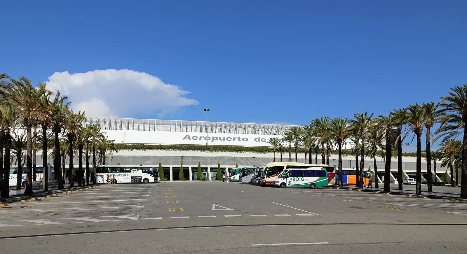 A wide aerial view shows Palma de Mallorca Airport's terminals, aprons, and surrounding Mallorcan landscape.