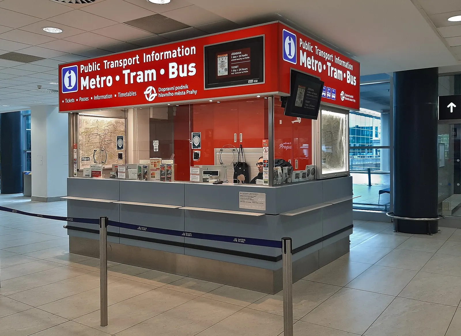 A public-transport information kiosk in the Terminal 2 arrivals hall at Václav Havel Airport Prague showing bus and metro route details.