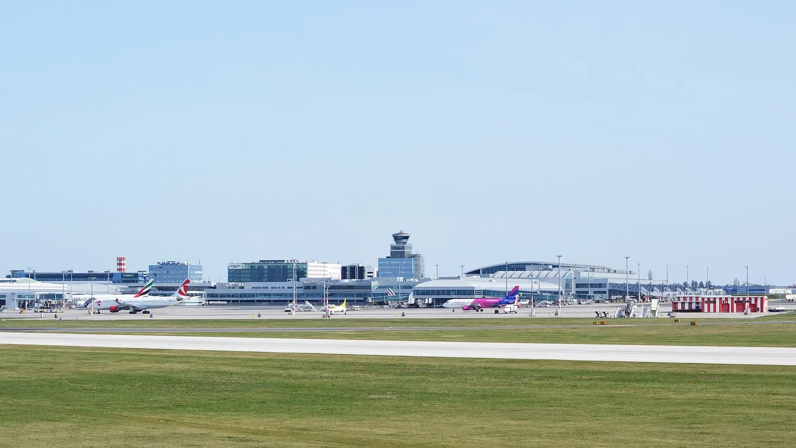 Wide exterior view of Prague Airport's passenger piers B and C with glass-fronted gate areas and aircraft parked at the stands.