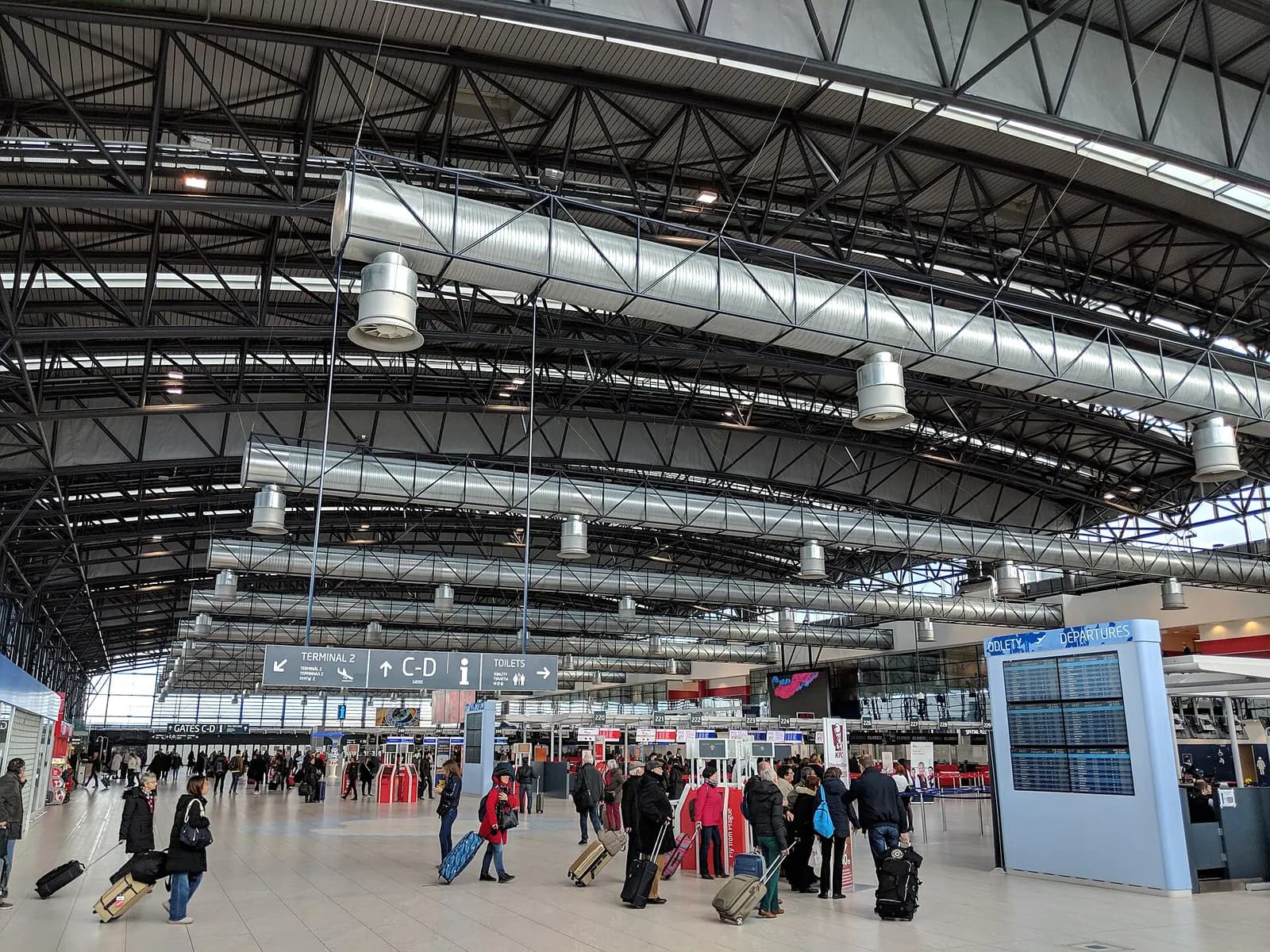 Spacious Terminal 2 departures hall at Prague Airport with check-in counters, departure boards, and travelers moving through the bright interior.