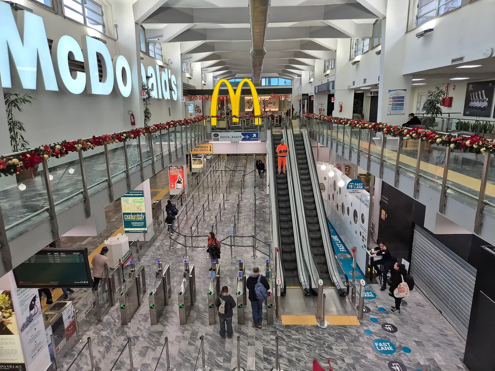 Another view of the upper-floor passenger hall at Pisa Airport with large windows and seating.
