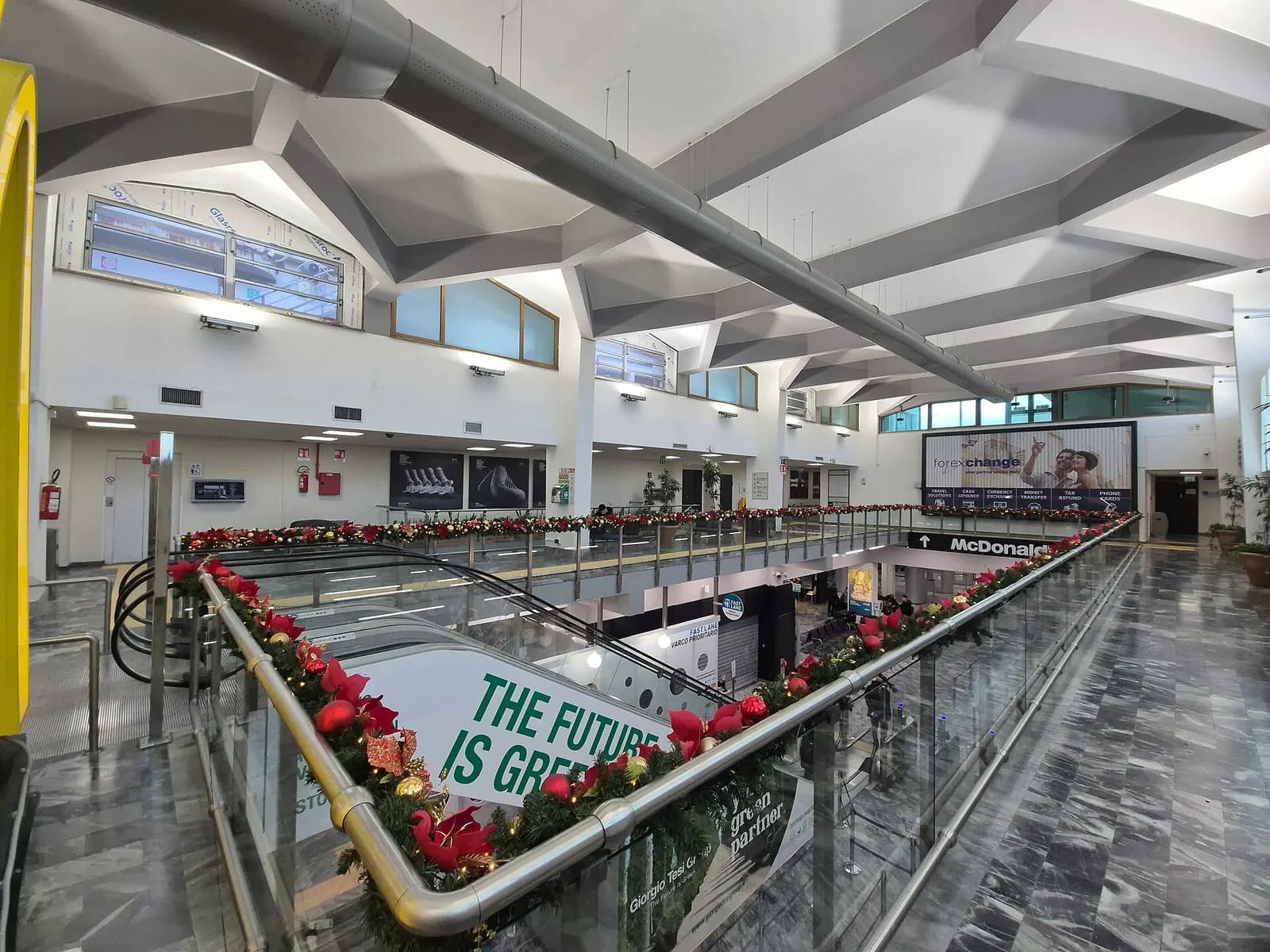 Upper-floor departures hall interior at Pisa Galileo Galilei Airport with seating and retail.