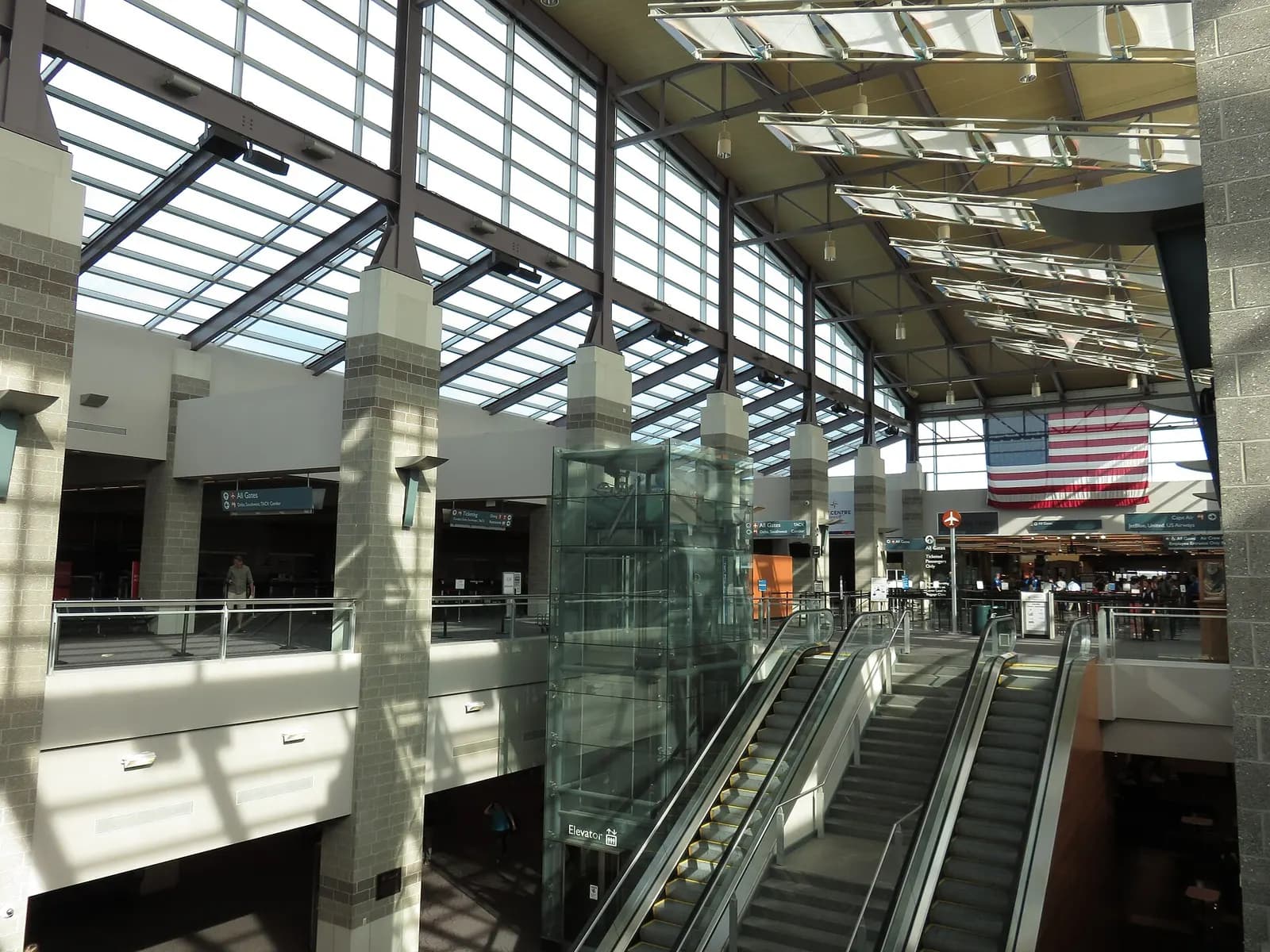 Skylit Bruce Sundlun Terminal lobby at T.F. Green, with the glass elevator and escalators between arrivals and departures.