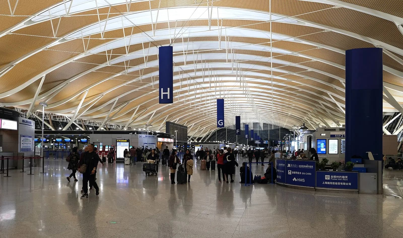 Wide view of the bright, spacious check-in hall at Shanghai Pudong International Airport with airline counters and travelers.
