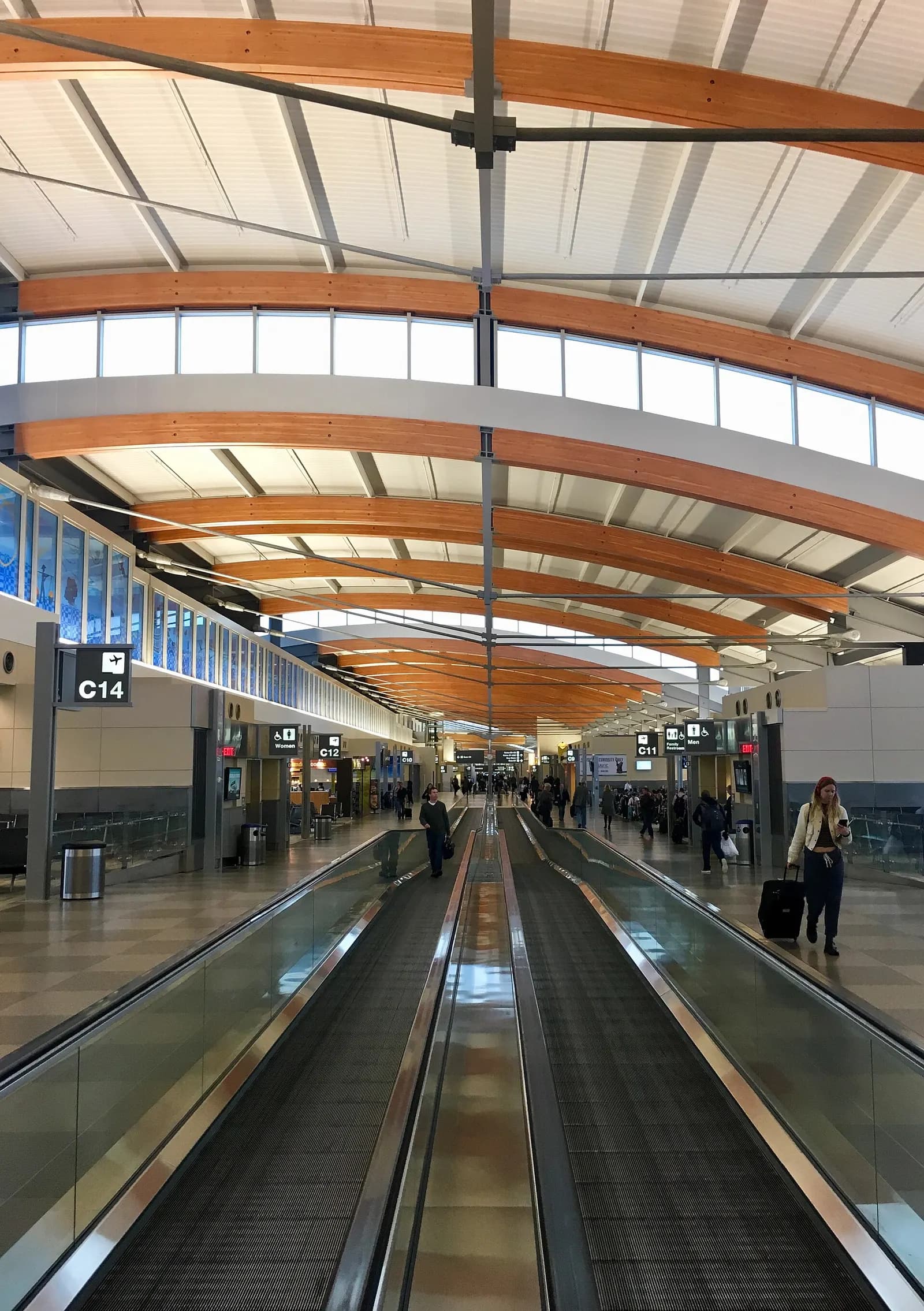 A long, bright concourse in RDU Terminal 2 with high ceilings, large windows, moving walkways, and gate seating areas along both sides.