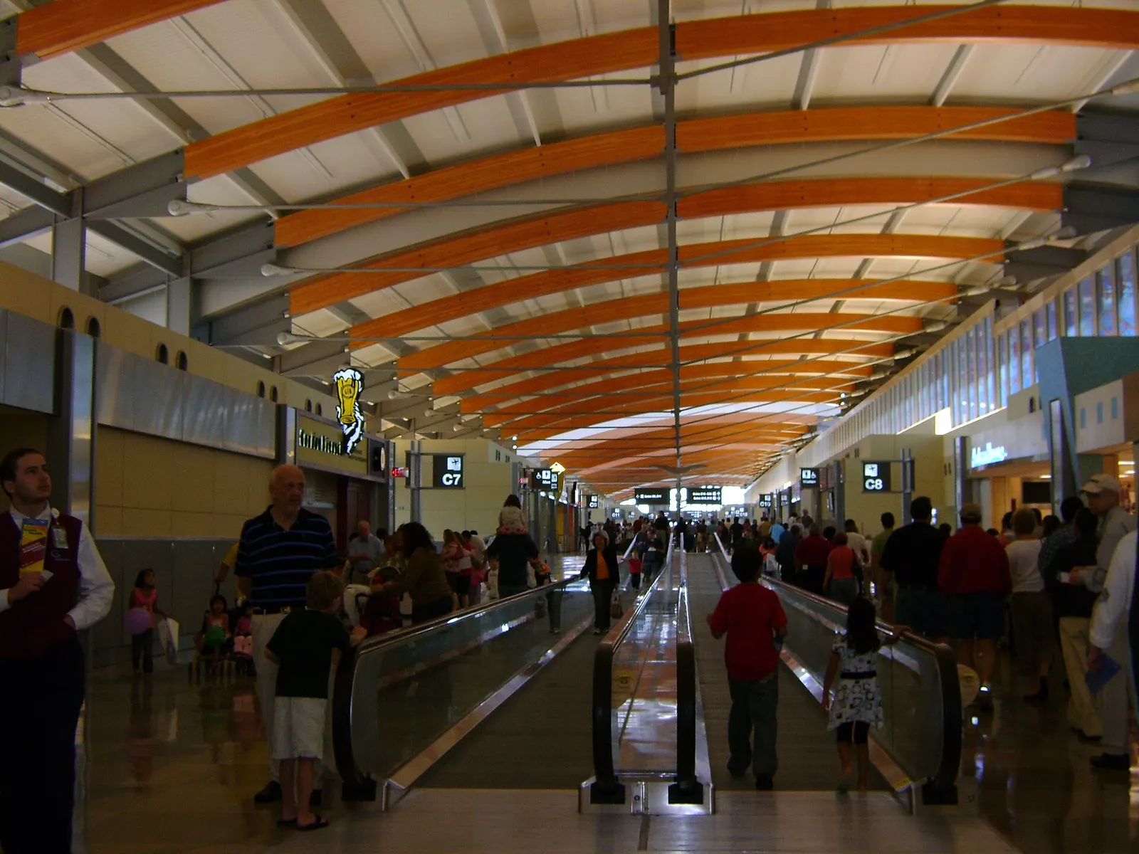 The inside of Concourse C in Terminal 2, showing the gate corridor, signage, seating, and large windows overlooking the airfield.