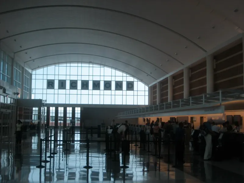 Landside ticketing hall at Richmond International Airport with RICHMOND lettering on the glass and passengers at the counters.