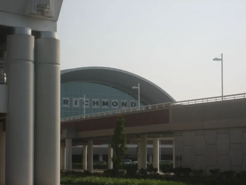 Curbside approach to the Richmond International Airport terminal, with the arched glass facade and RICHMOND lettering above the roadway.